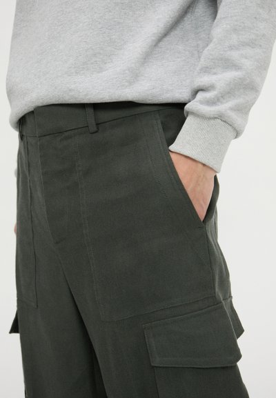 Dark green cargo pants with a smooth texture, featuring side pockets and a tailored fit, paired with a light grey sweatshirt.