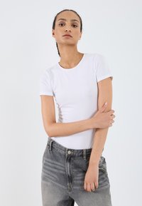 T-shirt blanc ajusté à manches courtes, associé à un jean en denim taille haute avec un dégradé du clair au foncé. Tissu lisse et col rond classique.