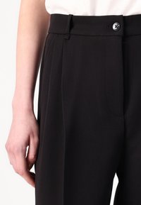 Black trousers with a tailored fit, featuring a visible button closure, pleats down the front, and a smooth, textured fabric.