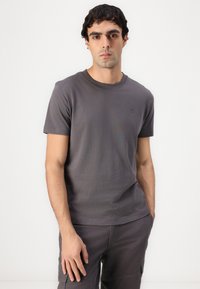 Graues kurzärmliges T-Shirt aus weichem Baumwollmaterial mit Rundhalsausschnitt und einem kleinen Logo-Detail auf der linken Seite. Glatte Textur, normale Passform.