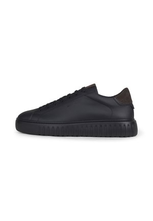 Schwarzer Sneaker mit niedrigem Schnitt, dicker profillierter Sohle, Schnürung vorne und dunkelbrauner Velours-Fersenlasche auf einfachem weißen Hintergrund.