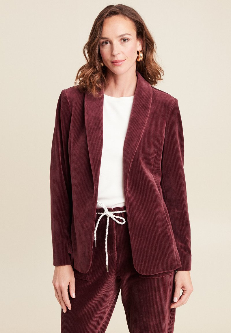 Burgunderfarbener Cord-Blazer mit Reverskragen, kombiniert mit einem weißen Oberteil und passenden Cordhosen mit Kordelzugbund.