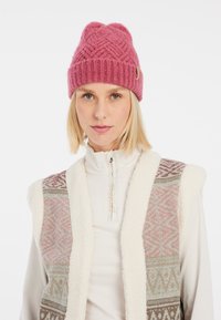 Rosa stickad mössa med ett strukturerat diamantsmönster, i kombination med en krämfärgad fleeceväst som har en geometrisk design i mjuka pastellfärger.