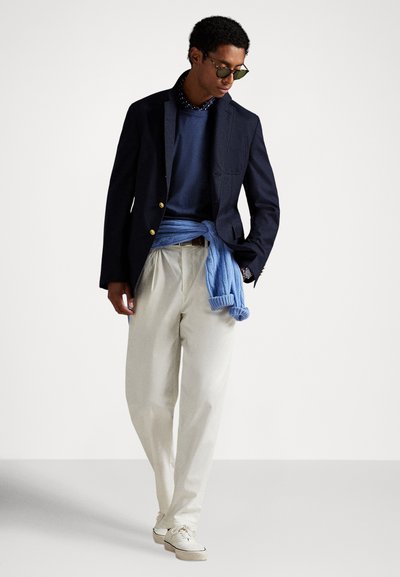 Tengerészblézer, kék kerek nyakú pulóver, világoskék kardigán deréknál megkötve, krémszínű pliszírozott nadrág és világos tornacipők.