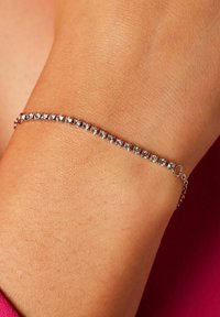 Pulsera de plata con cristales claros y redondos dispuestos en una línea recta. Cadena delicada con un cierre para un ajuste ajustable. Superficie lisa y reflectante.