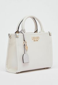 Sac à main en cuir blanc avec ferrures dorées, forme structurée, deux poignées supérieures et un porte-clés décoratif. Présente une bordure noire et un logo.