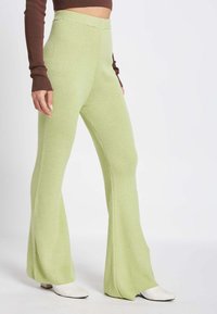 Geroeste, lichtgroene flaired broek met een hoge taille en verlengd silhouet; gecombineerd met witte puntige schoenen.