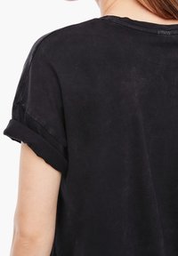 Camiseta negra de manga corta, hecha de algodón suave, con mangas enrolladas y un corte holgado. Tejido texturizado con un acabado desgastado.