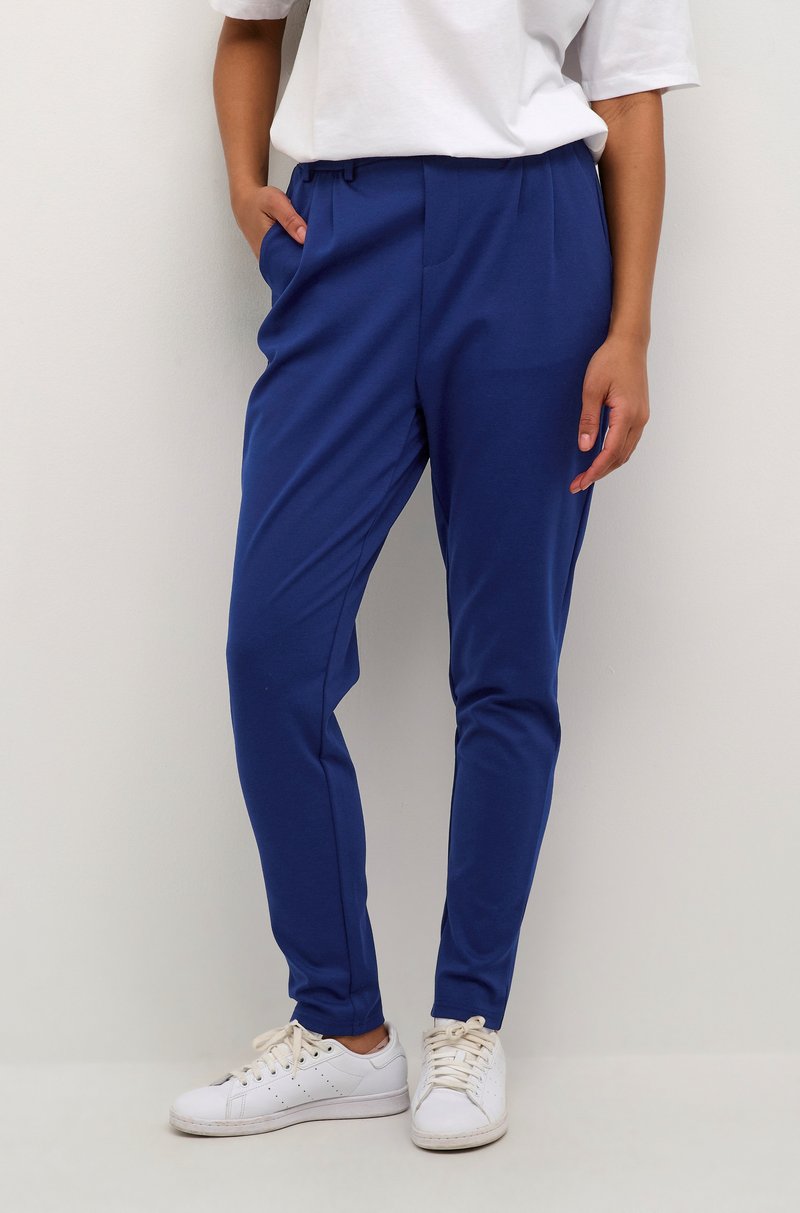Modré slim-fit kalhoty vyrobené z měkké tkaniny se bočními kapsami a stahovacími šňůrkami v pase, doplněné bílými teniskami.