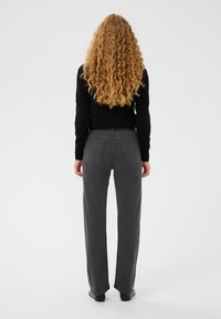 Sivé rovné džínsy s vysokým pásom, piatimi vreckami a čistým dizajnom na chrbte, v kombinácii s priliehavým čiernym svetrom.