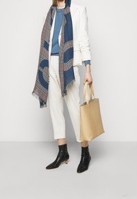 Blazer crème, sweat-shirt bleu, écharpe à carreaux avec franges, pantalon blanc, bottines noires et sac cabas beige. Mélange de textures et de couleurs.