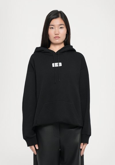 Sudadera negra con capucha, bolsillo frontal, cordón y un pequeño parche de logotipo blanco en el centro. Presenta mangas largas de corte holgado.