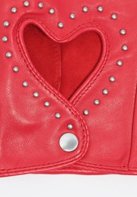 Accesorio de cuero rojo con un recorte en forma de corazón, tachuelas de metal gris y un botón a presión plateado, mostrando textura suave y costuras detalladas.