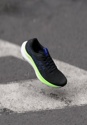 Scarpa sportiva nera con accenti blu e suola verde, caratterizzata da una tomaia testurizzata e lacci neri. Disegnata per la leggerezza e le prestazioni.