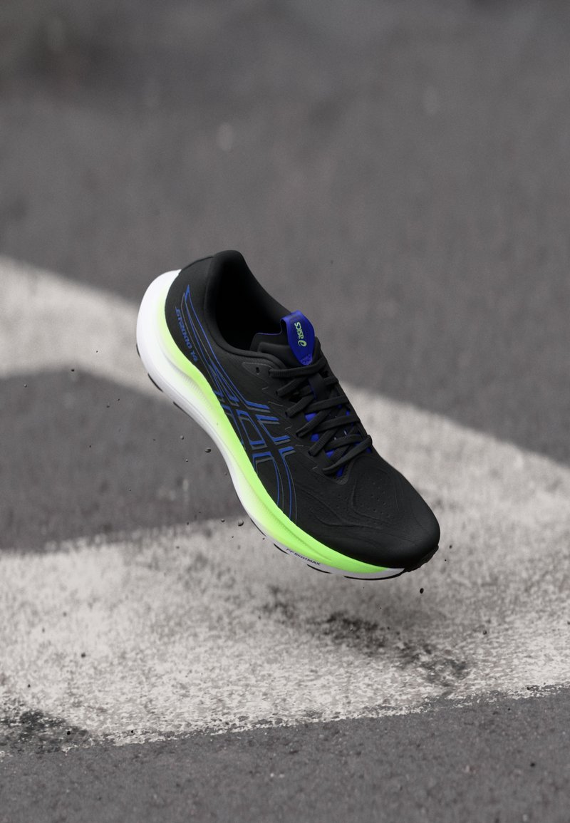 Zapato deportivo negro con acentos azules y suela verde, presenta un empeine texturizado y cordones negros. Diseño ligero para un mejor rendimiento.