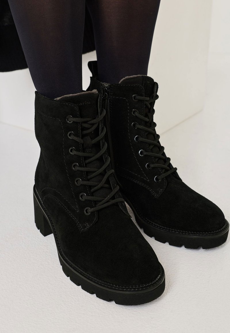 Black suede ankle boots with a lace-up front, a side zipper, textured surface, and block heels. Features stitching details and rubber soles.