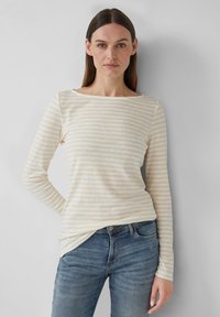 Striped long-sleeve top in soft cream and light beige fabric, featuring a wide neckline and a relaxed fit, paired with blue jeans.