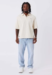 Polo a maglia color crema con colletto, con un motivo testurizzato. Abbinato a jeans azzurri e sneakers bianche, che mostrano un fit rilassato.