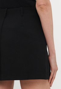 Zwarte shorts met een gladde textuur, voorzien van een strak ontwerp, zijzakken en een middelhoge tailleband. De achterkant toont de stiksel-details.
