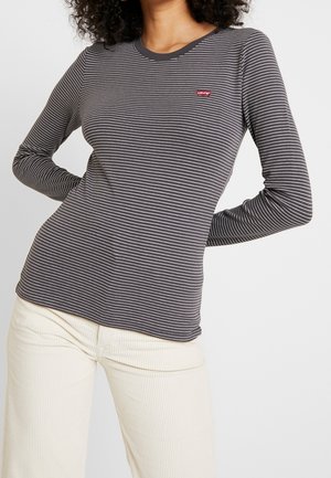 Femme portant un haut Levi's ajusté à manches longues rayé noir et blanc avec un pantalon en velours crème, vue des épaules aux hanches.