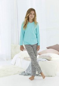 Turkizna majica z dolgimi rokavi, združena s pajkicami s črno-belim vzorcem. Postavljeno na svetlem ozadju z različnimi blazinami.