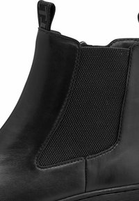 Musta nahkainen Chelsea-saapas, jossa on elastinen sivupaneeli, sileä pinta ja huomaamattomat ommel-yksityiskohdat. Pieni vetonauha takana.