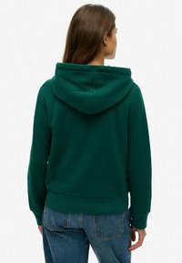 Donkergroen hoodie met een trekkoord, zachte textuur en geribbelde boorden. De achterkant toont een relaxte pasvorm en een kangoeroezak aan de voorkant.