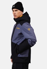 Herrenjacke im Color-Blocking-Design, mit grauen und schwarzen Paneelen, strapazierfähigem Material, verstellbarem Kapuzenkragen sowie Logo-Akzenten auf Brust und Ärmel.