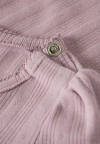 Tissu tricoté rose clair présentant une texture côtelée avec de petits motifs décoratifs, fini avec un bouton-pression argenté en accent.