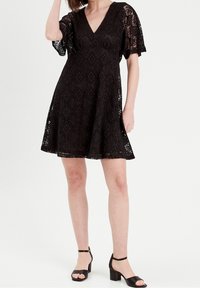 Robe en dentelle noire avec un col en V et des manches courtes bouffantes. Silhouette trapèze, présentant un motif floral complexe et une doublure.