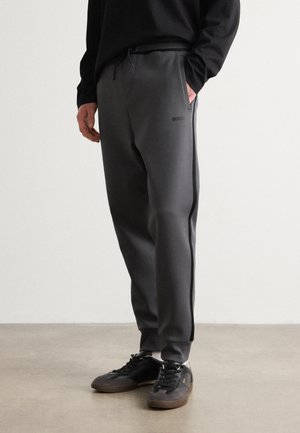 Grå sweatpants med en slät textur, med en dragsko i midjan, sidofickor och en logotypdetalj i svart. Kombineras med svarta sneakers.