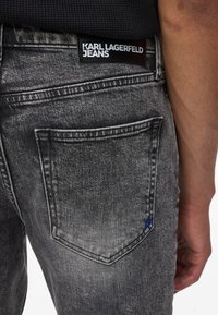 Karl Lagerfeld kavbojke v zbledelem črnem denim materialu, z usnjenim označbom na pasu in zadnjim žepom z modrim logotipom.