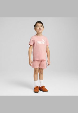 Rosa bomulls t-shirt med vit "PUMA" logotyp och matchande shorts, kombinerat med orange skor och vita strumpor, uppvisat mot en neutral bakgrund.
