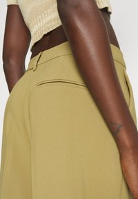 Ελαιόχρωμα ταγμένα παντελόνια με λεία υφή, διαθέτοντας πίσω τσέπη και σχεδίαση στενής εφαρμογής. Η ζώνη είναι φινιρισμένη με προσοχή.