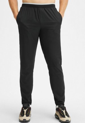 Zwarte sportieve broek in een taps toelopend ontwerp, vervaardigd van een soepele, lichtgewicht stof met een elastische tailleband en zijzakken.