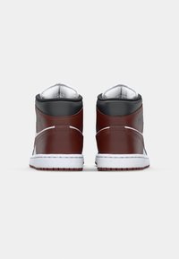 Ett par höga sneakers i brun, svart och vit sedd bakifrån mot en enfärgad ljusgrå bakgrund.