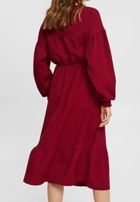 Robe bordeaux, longueur genou, avec de longues manches ballon, une taille cintrée et un ourlet à volants en couches. Fabriquée en tissu texturé.