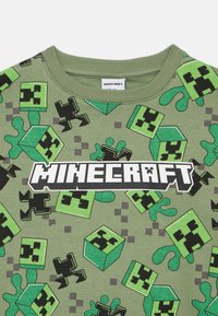 Zielony bawełniany sweatshirt z powtarzającym się wzorem w klimacie Minecraft, przedstawiającym twarze Creepera i bloki, z wyrazistym logo "MINECRAFT" w kolorze białym.