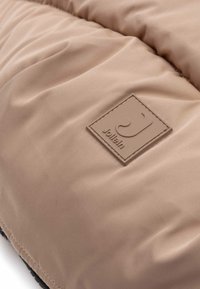 Tissubeige matelassé avec une texture lisse, featuring un patch logo rectangulaire en brun clair avec un design en relief.