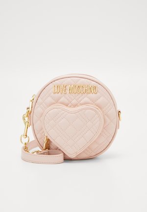 Kulatá růžová prošívaná crossbody taška s přední kapsou ve tvaru srdce, zlatými kovovými detaily a nastavitelným popruhem. Na tašce je značka vyražená zlatě.