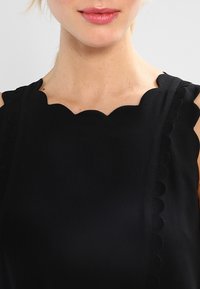 Robe noire avec un col en dentelle et des détails texturés le long des bretelles. Le tissu semble lisse et léger.