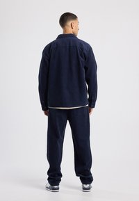 Navy corduroy jacket with matching trousers. The jacket features a collar and button closures, and the pants have a relaxed fit.