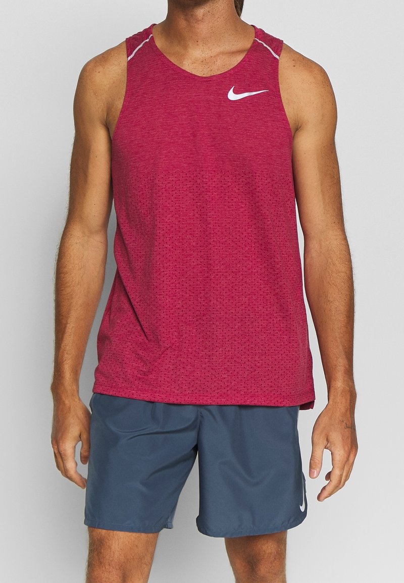 Rotes Sporttanktop mit kleinen Perforationen, weißem Nike-Logo, kombiniert mit grauen Shorts aus feuchtigkeitsableitendem Material.