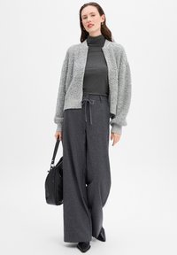 Light gray, textured knit cardigan over a dark gray turtleneck; wide-leg dark gray pants; black handbag; pointed black shoes.