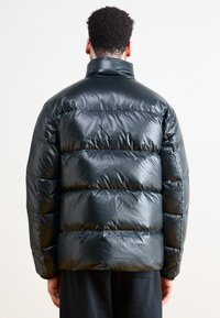 Chaqueta tipo puff en material negro brillante, con un cuello alto, diseño acolchado y un giro suave para aislamiento.