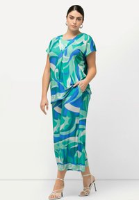Tenue fluide et multicolore avec des motifs tourbillonnants dans les verts et les bleus, comprenant un col en V et des manches courtes, complétée par un pantalon et des talons à lanières.