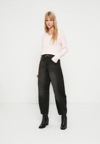 Camisola rosa claro de manga comprida com decote em V, combinada com jeans cinza escuro de cintura alta e botas pretas de salto até ao tornozelo. Design simples, detalhes mínimos.