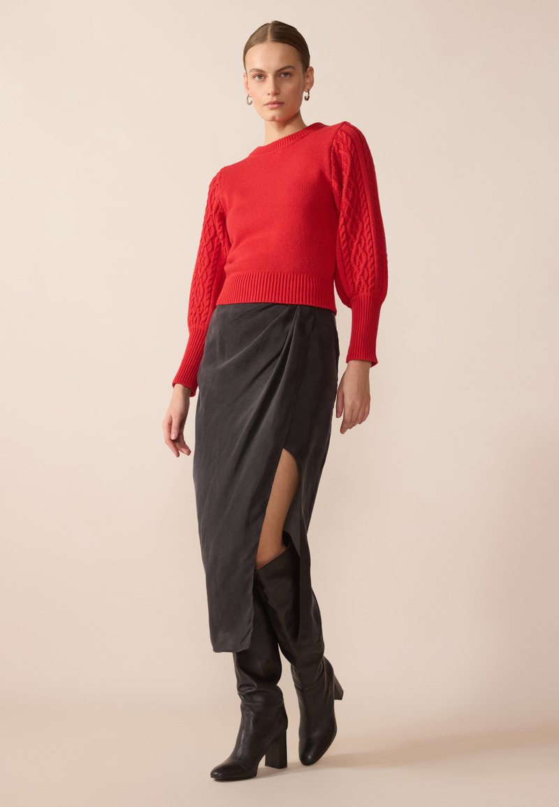 Czerwony sweter z dzianiny o fakturowanych rękawach, w połączeniu z czarną spódnicą z wysokim rozcięciem. Całość dopełniają czarne kozaki do kolan.