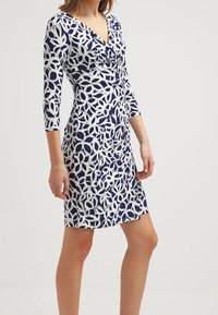 Navy blue dress with a white floral pattern, featuring three-quarter sleeves, a V-neckline, and a fitted silhouette. Smooth texture.