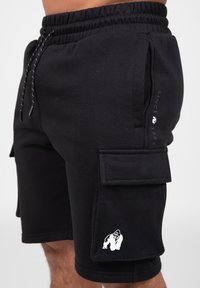 Black cotton shorts with elastic waistband, drawstrings, and two side pockets. Features a patch pocket and a white gorilla logo on the leg.